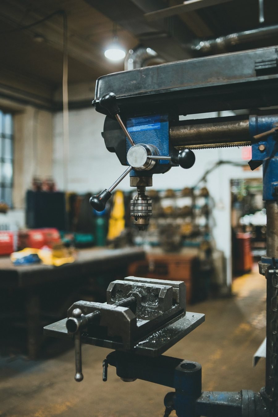 A pedestal drill press with a vise on its table in a cluttered shop