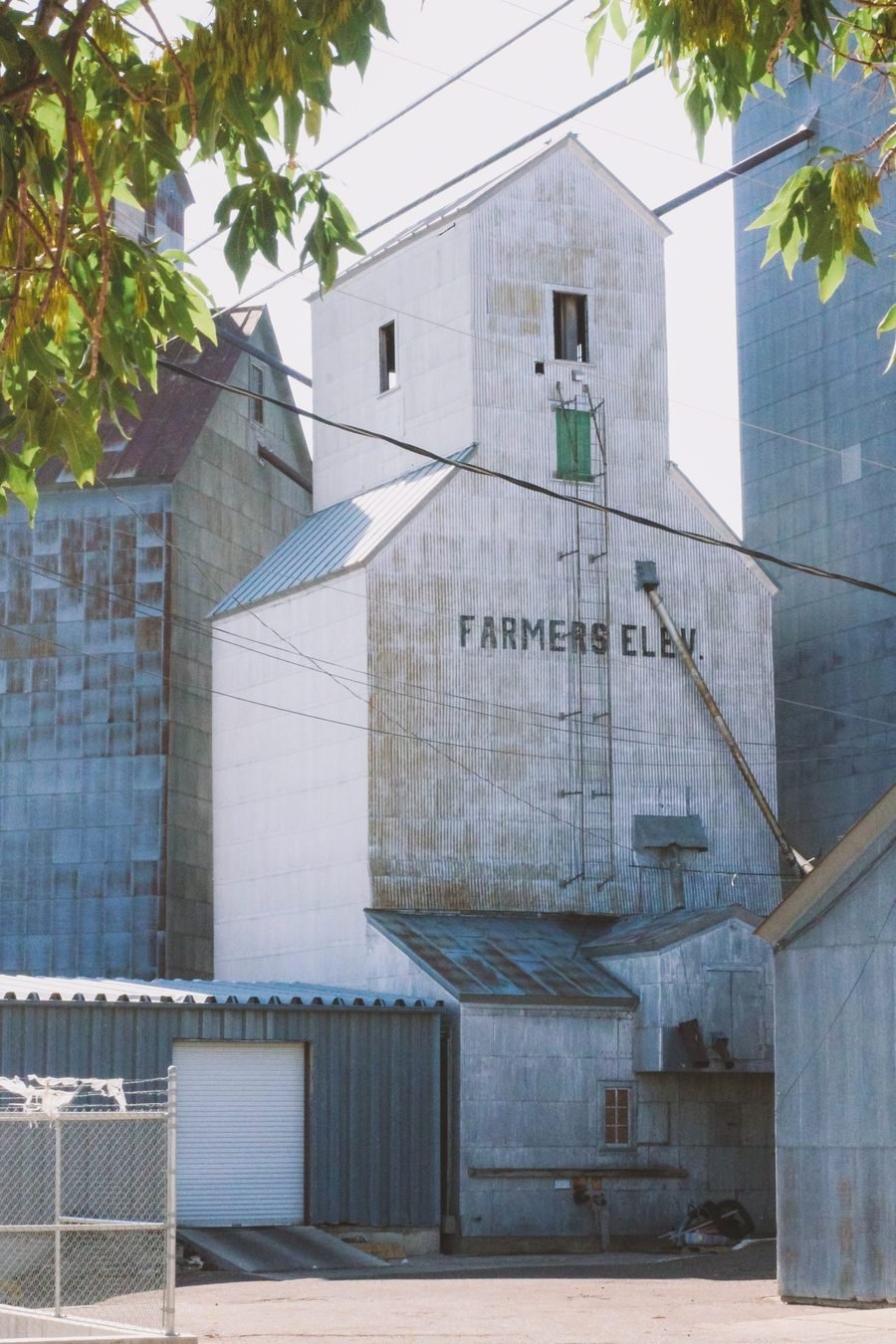 A tall corrugated farmers grain elevator behind a chain-link fence