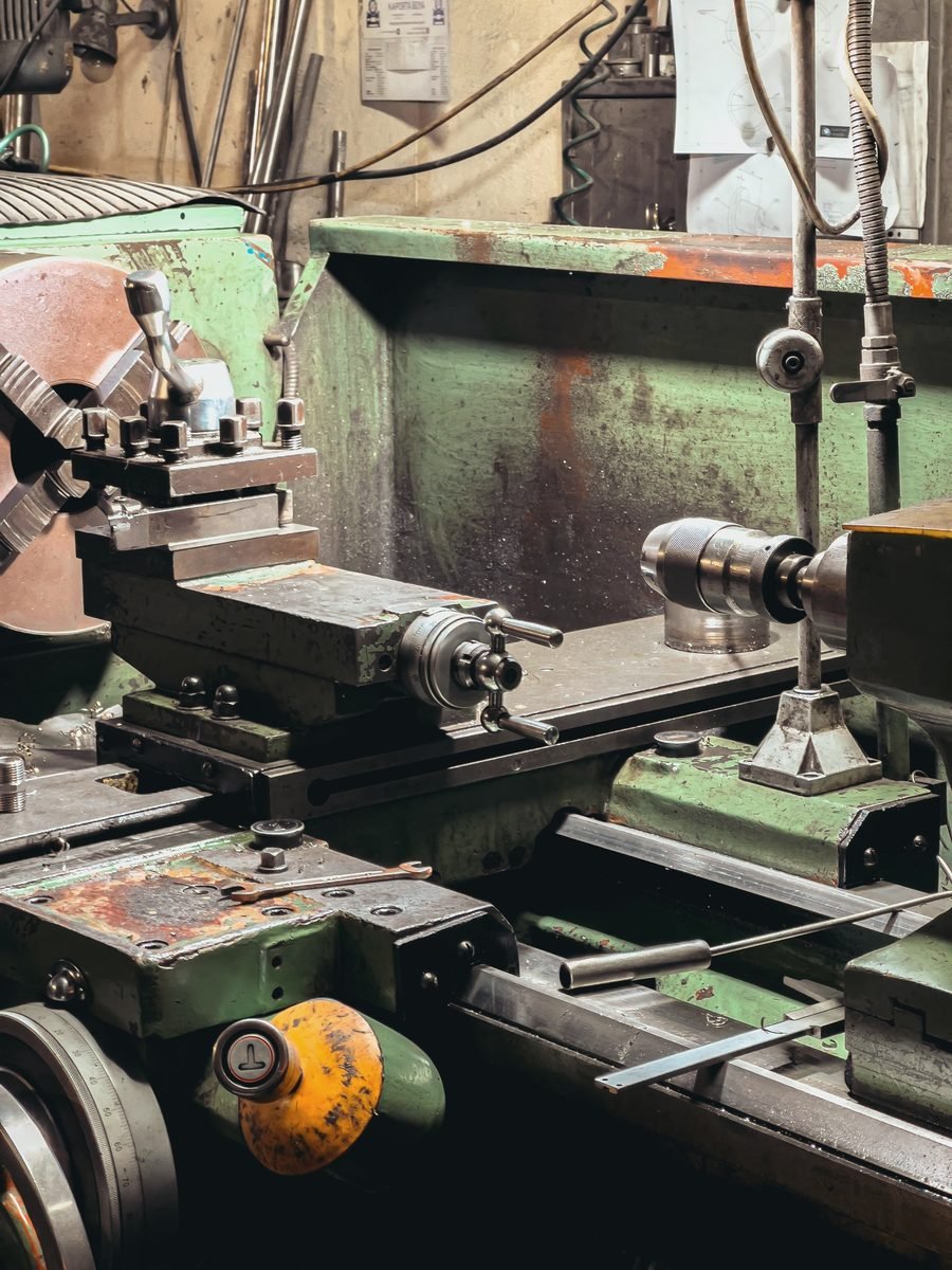A worn green lathe with a cross slide and tool post in a working shop