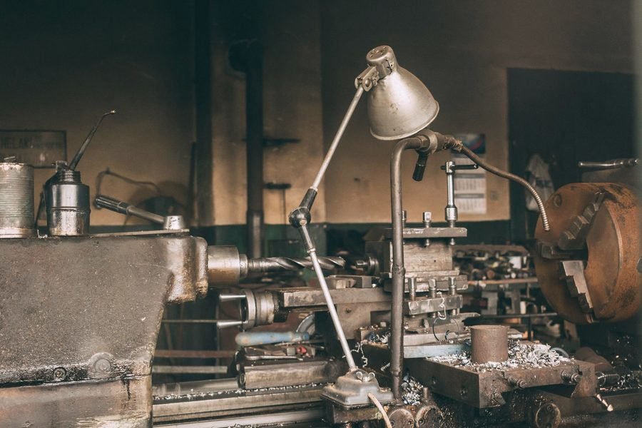 An old engine lathe under a bent-arm work lamp, chips piled on the carriage