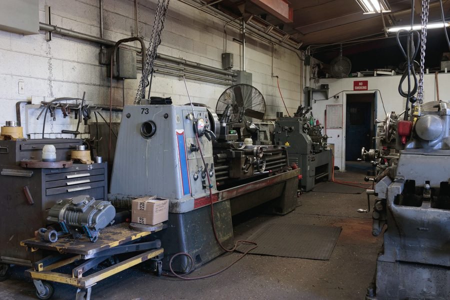 A long machine shop with engine lathes, rolling carts and chain hoists along a block wall