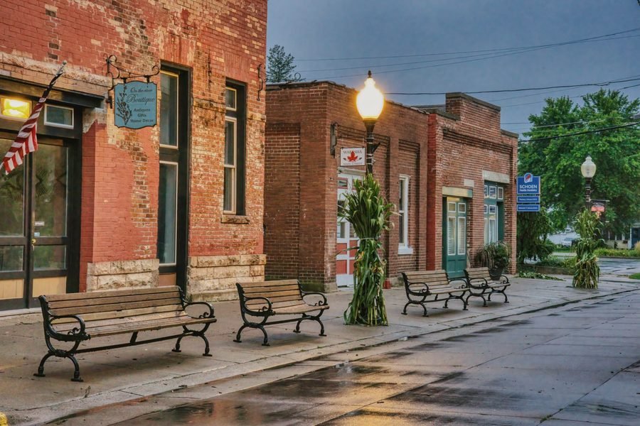 Brick storefronts and park benches along a wet small-town main street on an overcast morning